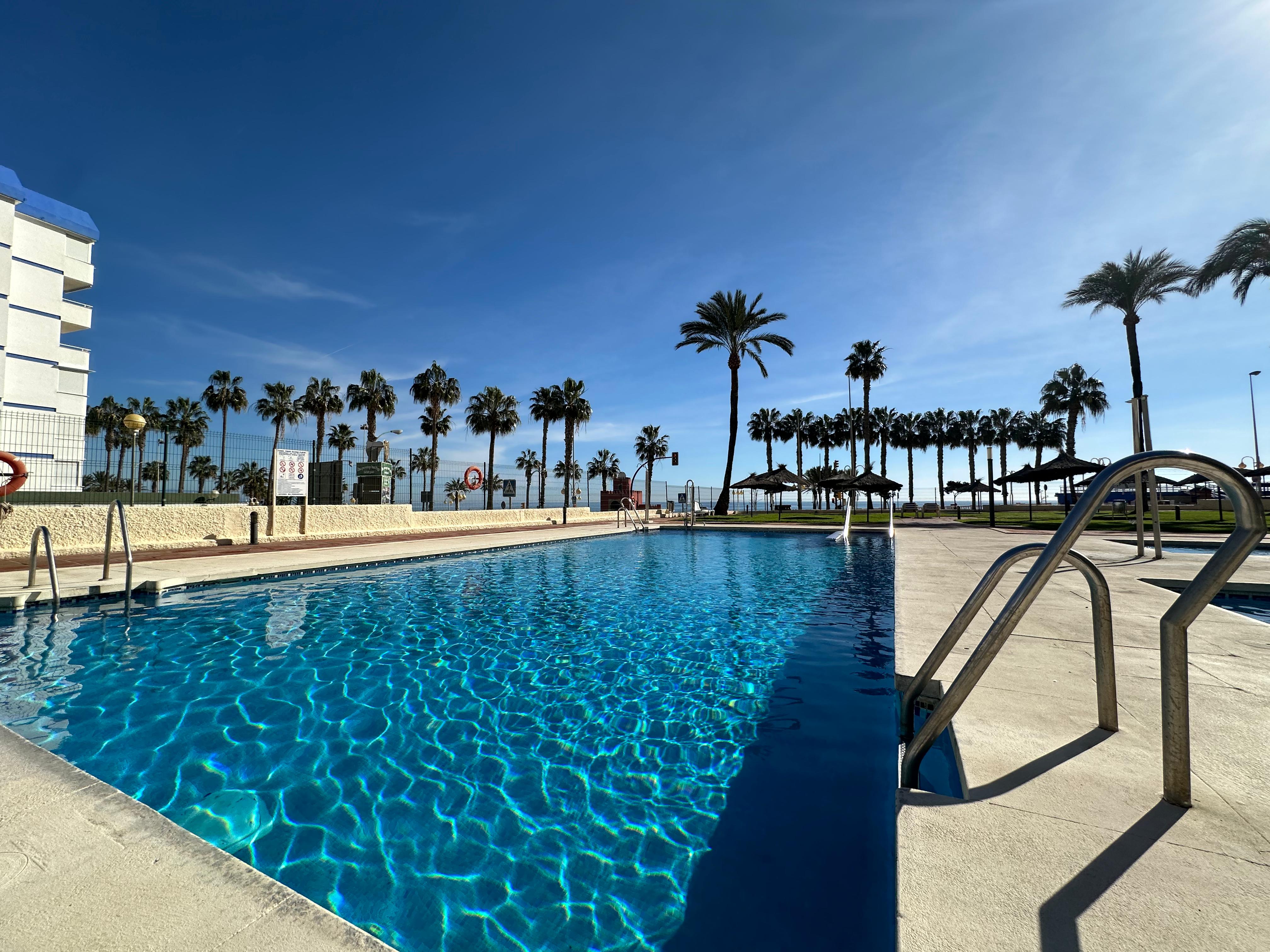 Piscina comunitaria con palmeras junto al mar de un apartamento turístico en Benalmádena