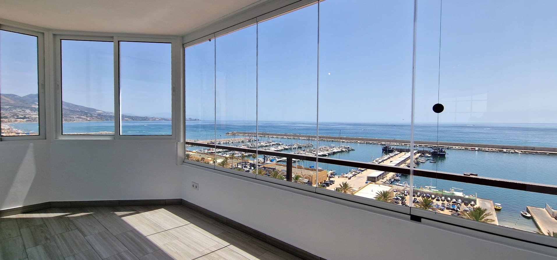 Terraza acristalada de un apartamento turístico en Fuengirola con vistas al puerto deportivo y al mar